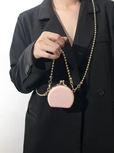 Close-up van roze ronde tas met kushes en gouden kralenketting, modieuze detailopname.