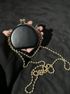 Detailgezicht van de zwarte mini-kiss-lock tas met een stijlvolle gouden kogelketting-schouderriem.