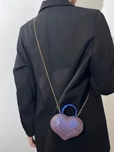 Vista dettagliata della borsa a tracolla con cuore in strass brillanti, manico blu e catena d'oro.