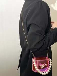 Borsa box in acrilico rosa con manico di perle e catena metallica, dettagli eleganti.