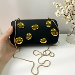 Nahaufnahme der schwarzen Acryl-Clutch Tasche mit glänzenden goldenen metallischen Akzenten.