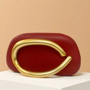 Detail view of the red mini evening bag featuring an oversized gold curved metal handle design.