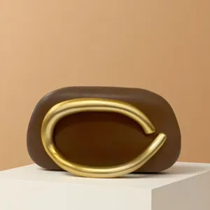Close-up of mini brown leather shoulder bag featuring a striking gold metal circular handle.