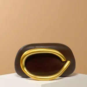 Close-up detail of a dark brown mini clutch bag featuring a prominent gold metal ring handle.