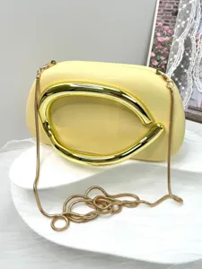 Detailed view of elegant yellow evening clutch bag featuring sculptural gold metallic handle