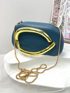 Detail shot of womens blue clutch bag with large gold metal handle and chain strap.