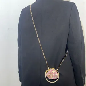 Detail view of a mini rhinestone evening bag with gold chain strap worn over a black blazer.