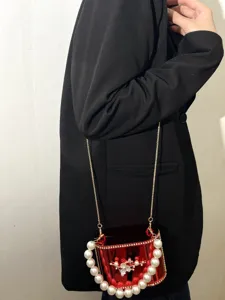 Dettaglio borsa a scatola in acrilico rosso con manico di perle e tracolla a catena.