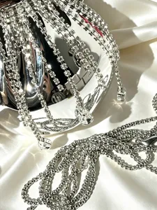 Detailaufnahme einer Strass-Quasten-Tasche, glänzende Silberkristallketten und Metallriemen auf Satin.