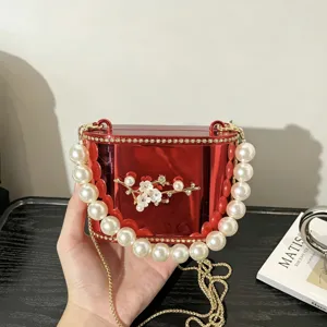Dettaglio della borsa rigida in acrilico rosso con manico di perle e decoro floreale.