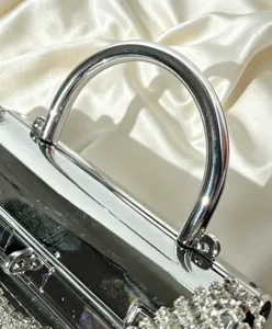 Details einer silbernen Acryl Abendtasche mit poliertem Metallgriff und funkelnden Strasssteinen.