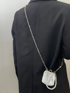 Detail view of a mini lace kiss-lock crossbody bag featuring stylish chain and pearl straps.