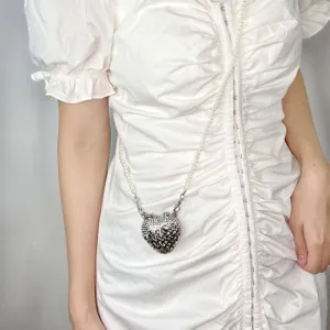 Detailaufnahme einer mini strassverzierten herzförmigen tasche mit edler perlenkette.