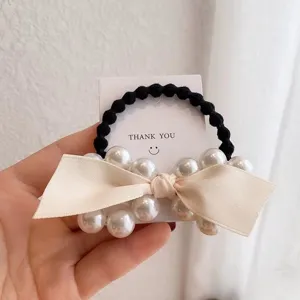 Close-up detail of the elegant black hair tie featuring faux pearls and a chic beige bow.