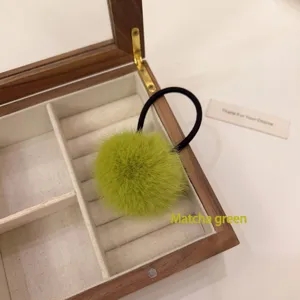 Close-up detail of the matcha green fluffy fur ball hair tie with elastic band in wooden jewelry box.