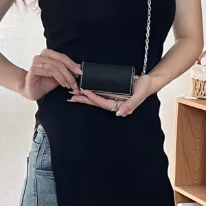 Gros plan sur le mini sac porte-cartes en cuir noir avec chaîne métallique argentée.