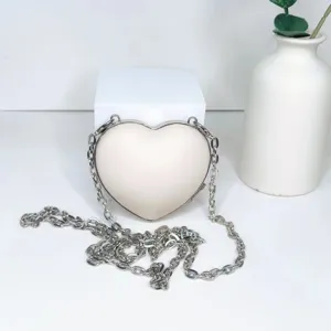 Detailansicht einer niedlichen herzförmigen Mini-Umhängetasche mit metallischem Kettenriemen.