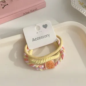 Detailed view of braided hair ties set with orange charm on white card, clean pastel style.
