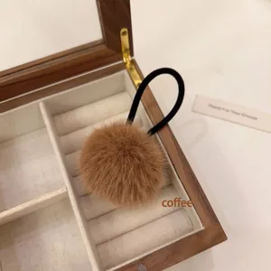 Close-up detail of fluffy brown pompom hair tie displayed neatly in a vintage wooden jewelry box.