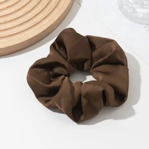 Detailed shot of a brown satin hair scrunchie, smooth texture, elegant daily hair accessory.