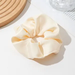 Close-up detail of a soft beige satin hair scrunchie showing smooth fabric texture.