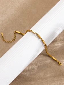 Bracelet de maillons barres en acier dore, vue de detail elegante sur support blanc texture.