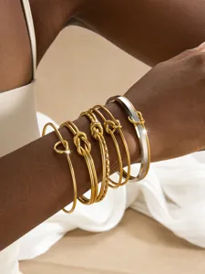 Detailaufnahme eines mehrschichtigen goldenen Knotarmband-Sets, minimalistischer Schmuck.