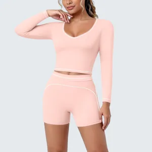 Close-up detail of the pink long-sleeve crop top and shorts yoga set with white piping trim.
