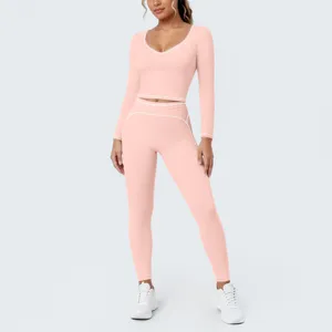 Detailed view of women's pink long sleeve crop top and leggings yoga set with white piping.