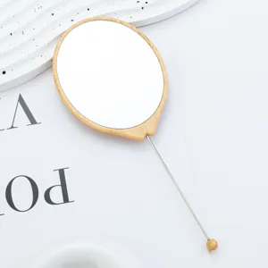 Specchio da trucco portatile ovale in legno con asta in metallo e ciondolo per uso quotidiano.