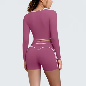 Back view of women's long sleeve crop top and shorts yoga set in mauve with white piping.