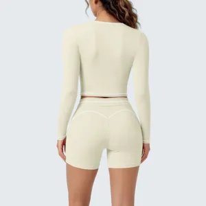 Detail view of women two-piece yoga set, beige long sleeve top and shorts with white piping.
