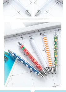 Detail shot of clear barrel ballpoint pens with Christmas patterns and metal tips on grid background.
