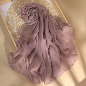 Close up of a dusty pink shimmer hijab scarf on a wooden tray with woven mat detail.