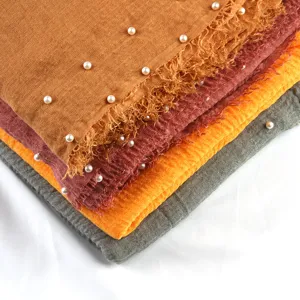 Close-up detail of folded crinkled cotton linen scarves with pearl beadings and fringed edges.