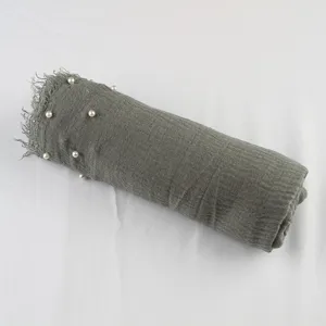 Closeup detail view of the crinkly cotton linen scarf texture, featuring pearl studs and fringe edge.