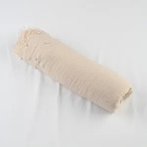 Detail view of a beige pleated cotton linen scarf with pearl beaded fringe for elegant styling.