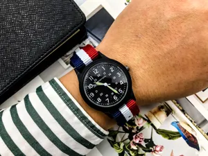 Detail view of nylon military watch featuring a black dial, luminous hands, and striped strap.
