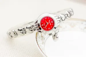 Élégante montre bracelet quartz pour femme avec cadran rouge, maillons cœur et charm.