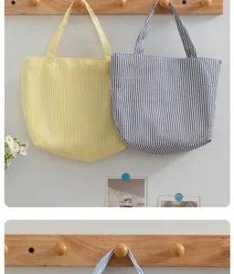 Closeup of stylish striped canvas tote bags hanging on wooden rack, casual summer design.