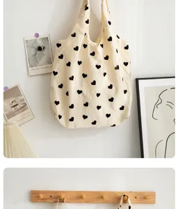 Close-up view of a beige canvas shoulder bag featuring allover black heart print pattern.