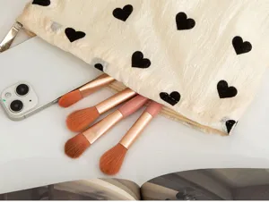 Close-up detail of plush heart pattern makeup pouch showing soft texture and brushes.