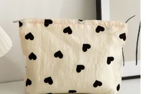 Beige canvas cosmetic bag with black heart print, portable zipper makeup pouch for travel.