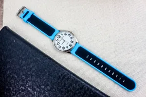 Silicone quartz watch detail view, blue and black strap, clear numbers on white dial.