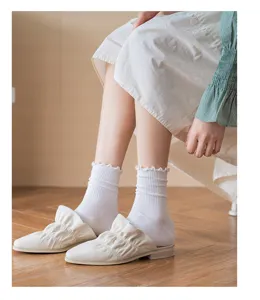 Detail shot of white ruffled mid-tube socks paired with pleated casual slip-on shoes indoors.