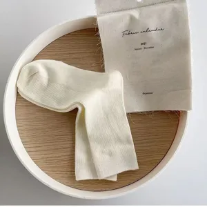 Cremeweiße gerippte Mittelsocken, feine Doppelnabenstrick-Textur, minimalistische Detailansicht.