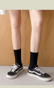 Close-up detail shot of casual solid black mid-calf cotton socks worn with sneakers.