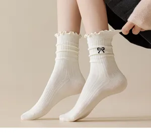 Detailed shot of white ribbed ruffle socks with cute black bow embroidery, soft knit.