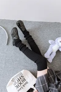 Details of black knit leg warmers paired with loafers and plaid skirt, y2k aesthetic style.