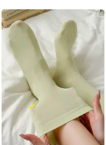 Gros plan de chaussettes mi-mollet en coton vert clair avec une texture côtelée sur lit blanc.